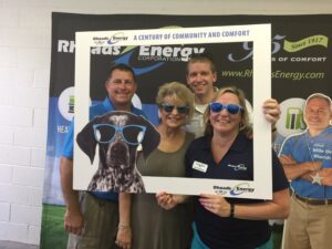 A group of individuals takes a selfie with a branded selfie frame and fun sunglasses.