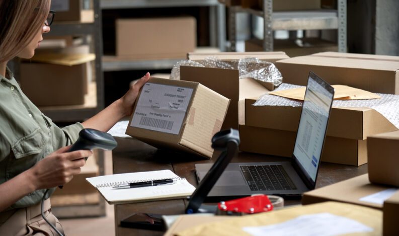 A female worker reads a shipping label while holding a barcode scanner.