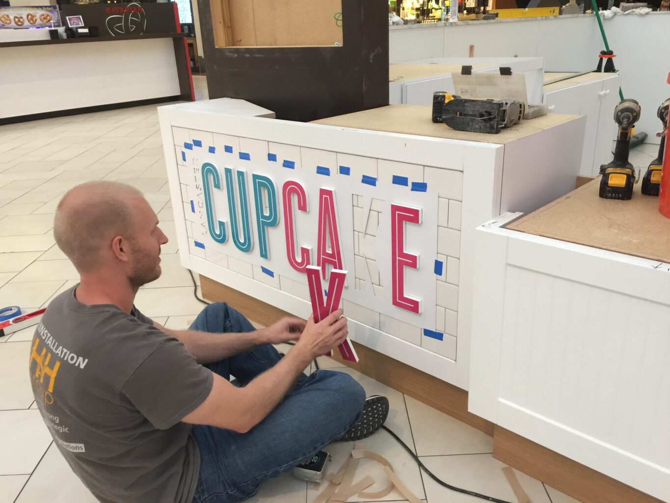 An employee from The H&H Group installs interior signage for a cupcake company.