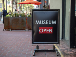 A black sidewalk sign with white text that reads museum open.