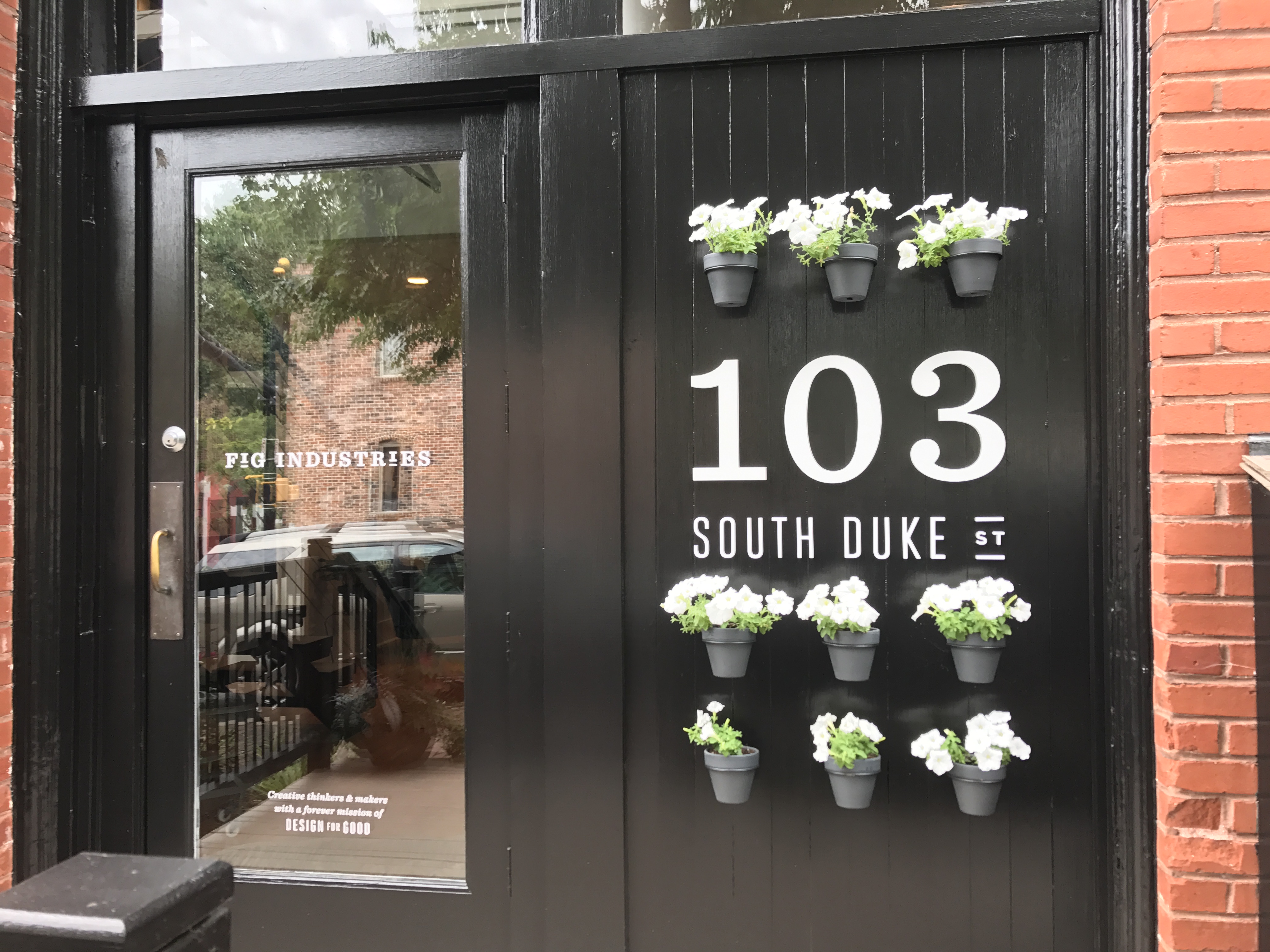 An image with an outdoor business address sign that has flowerpots around it