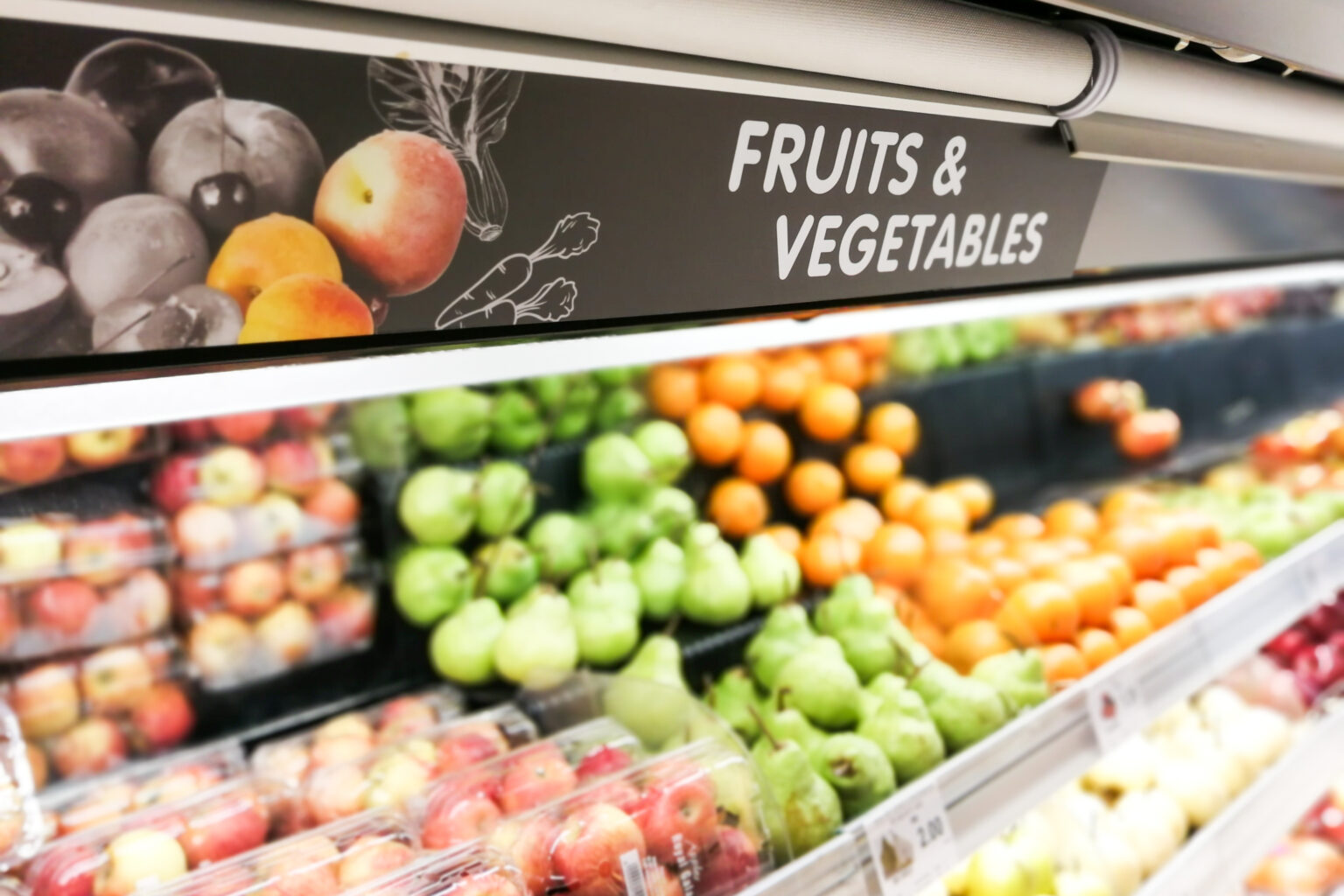 A sign that says “Fruits and Vegetables” hanging over the fruits and vegetables section at a grocery store.