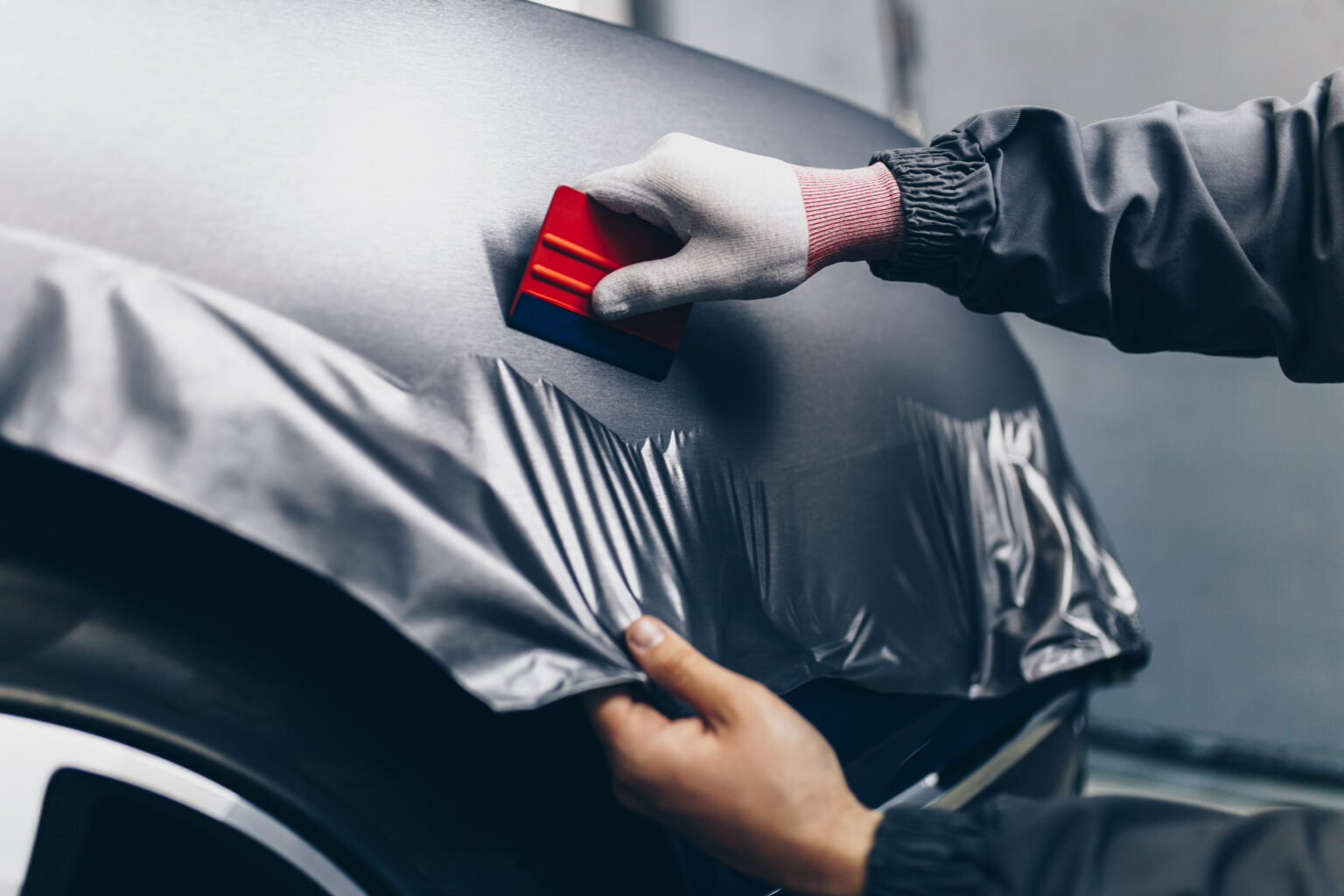 A person applies a vehicle wrap with a red tool.