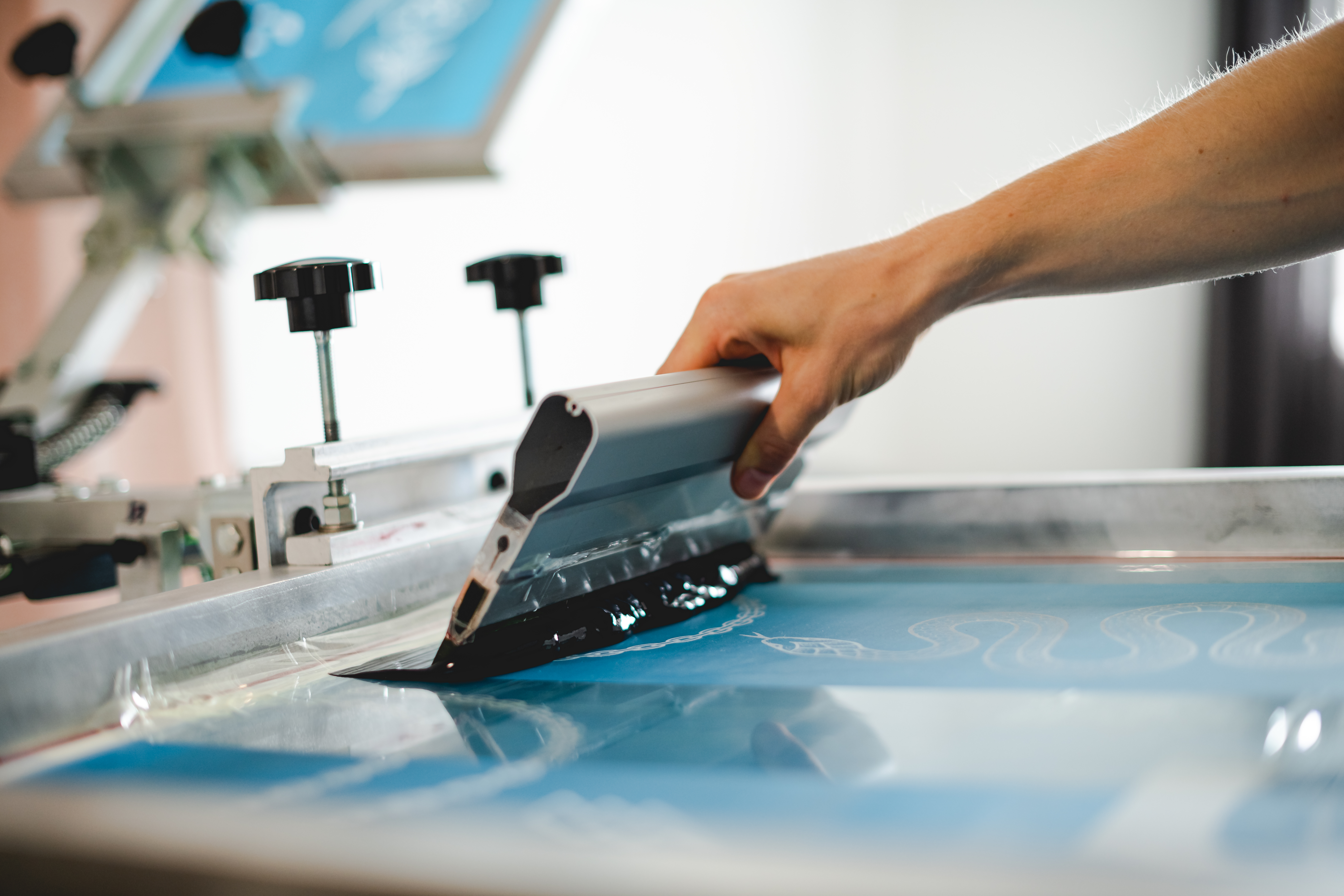 A person is screen printing something with blue ink.